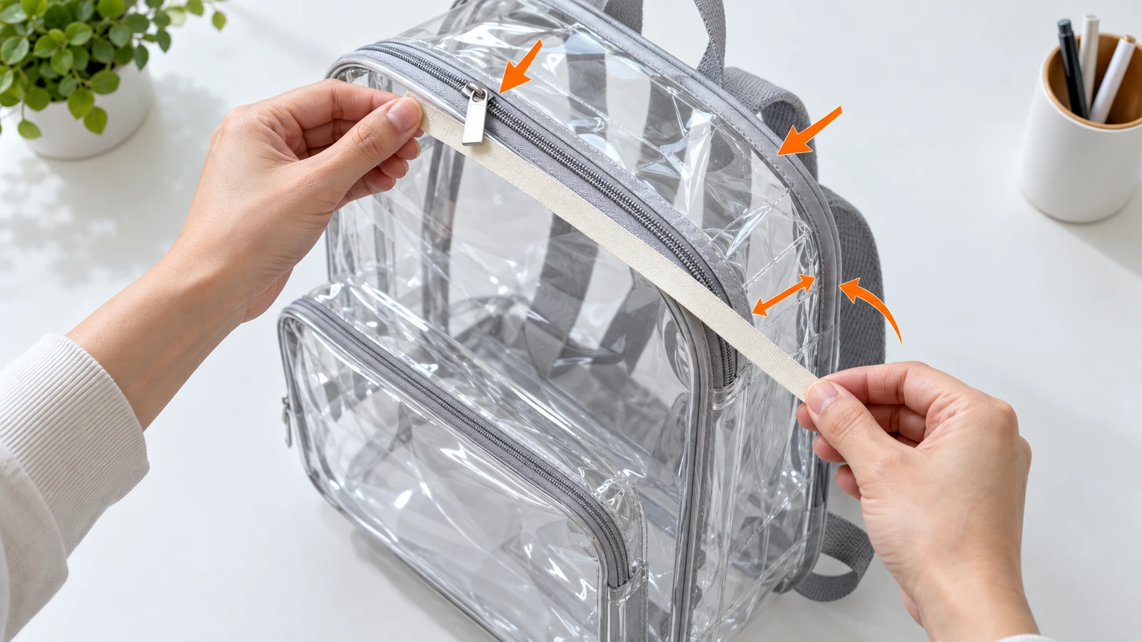 Mãos medindo a altura externa, a largura e a profundidade do fole de uma mochila de PVC transparente com uma trena simples, com setas indicando que os cursores do zíper e o acabamento entram na medição do tamanho
