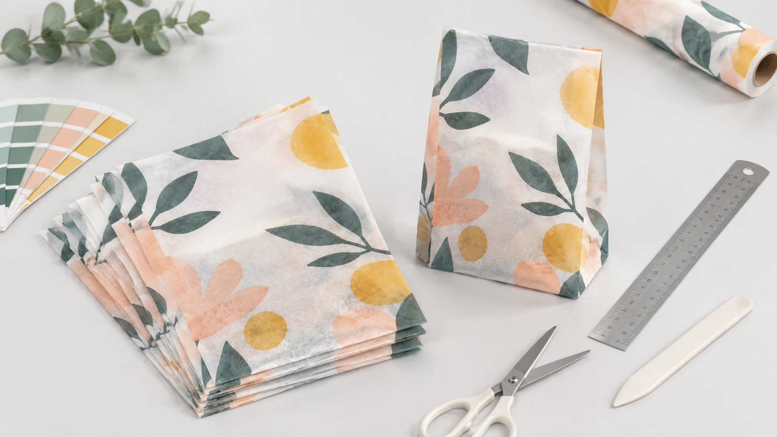 Sacolas de papel com estampa floral e materiais para confecção de amostras Sacolas de papel translúcido com estampa floral, acompanhadas de rolo de papel, régua, tesoura e amostras de cor