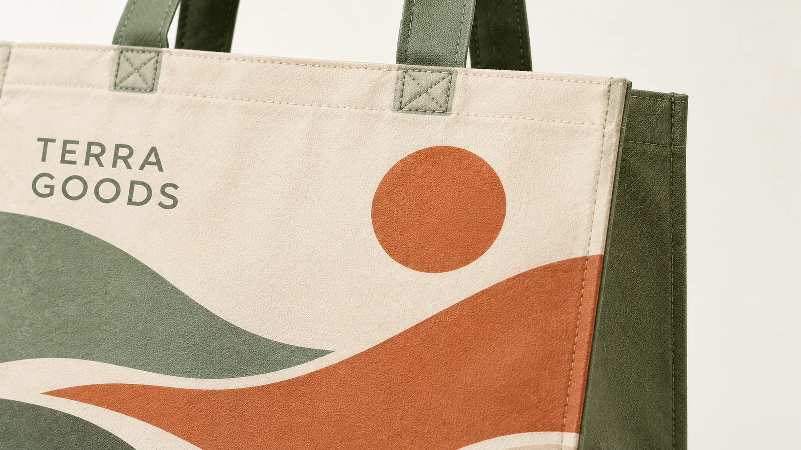 Close-up de uma sacola tote com estampa de paisagem, texto TERRA GOODS e alças verdes costuradas