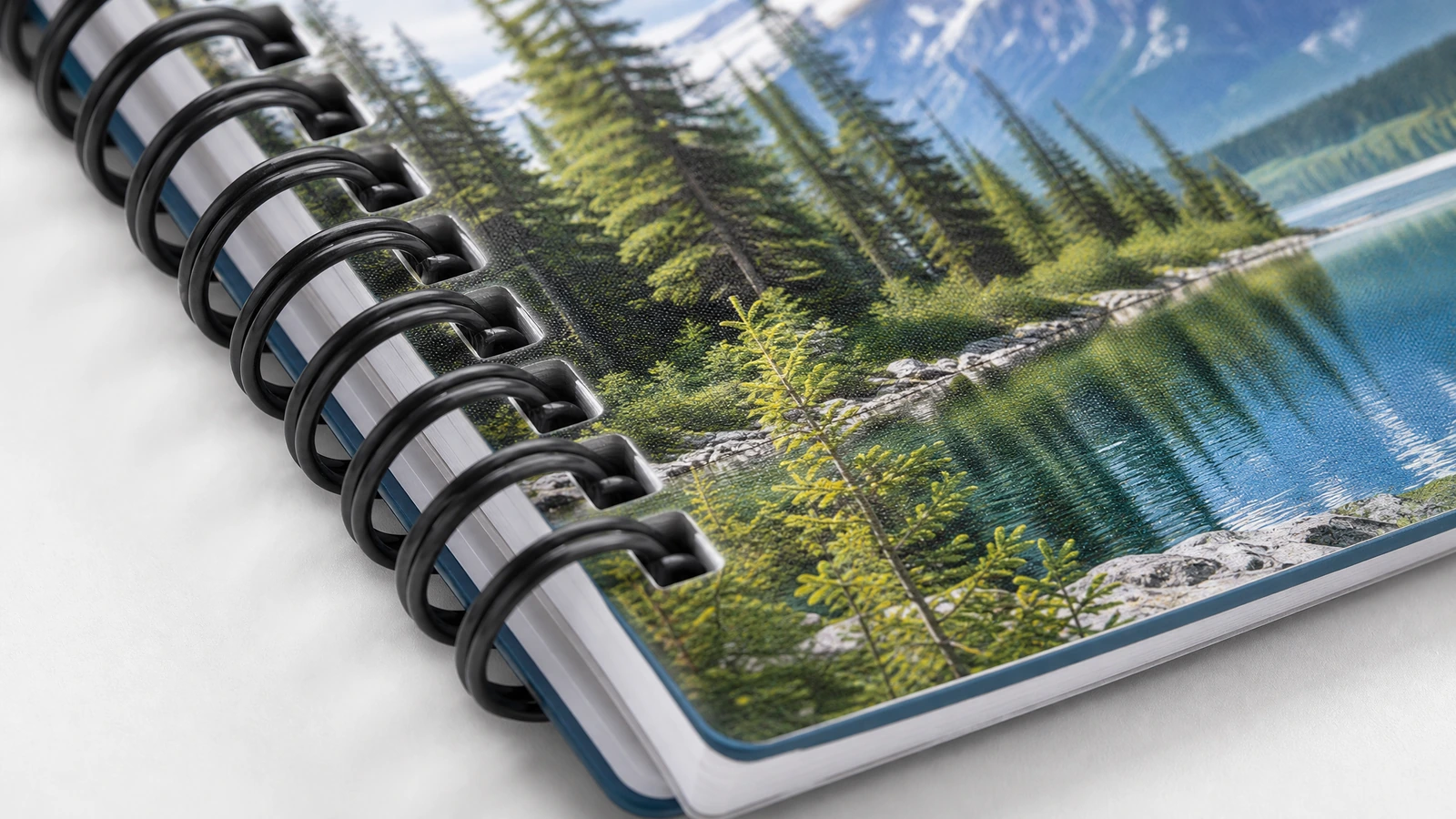 Ilustração em close-up da encadernação de um caderno preto e da capa com paisagem de lago montanhoso impressa