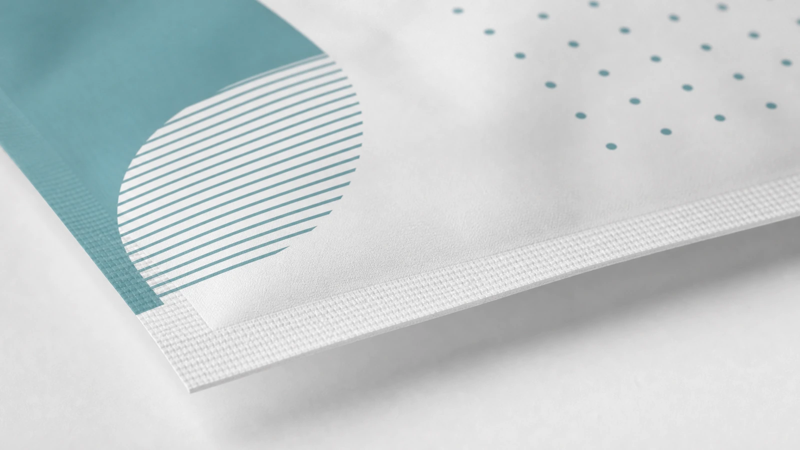 Detalhe da impressão e da borda selada da bolsa Close-up da estampa geométrica azul-petróleo e da borda selada texturizada de uma bolsa branca